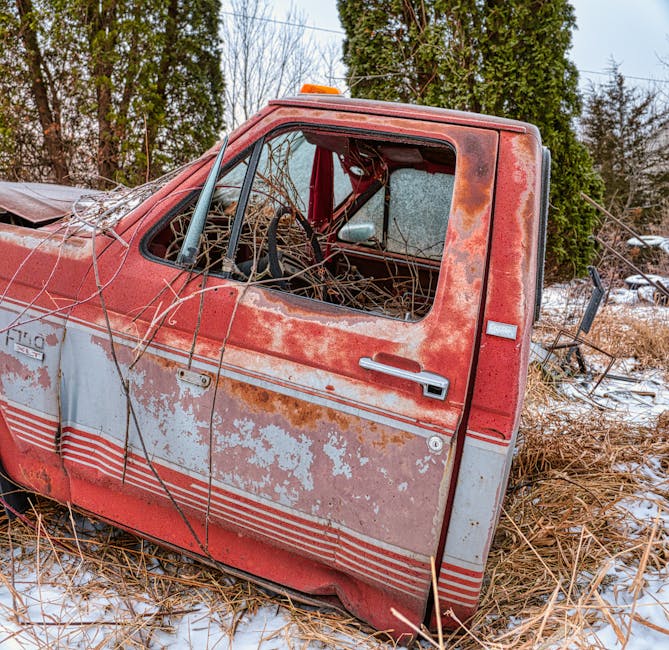 A vintage cream-colored van driving along a paved road, loaded with various household furniture and items in the back cargo area. The load includes wooden chairs, a small table, and a plastic bag, all